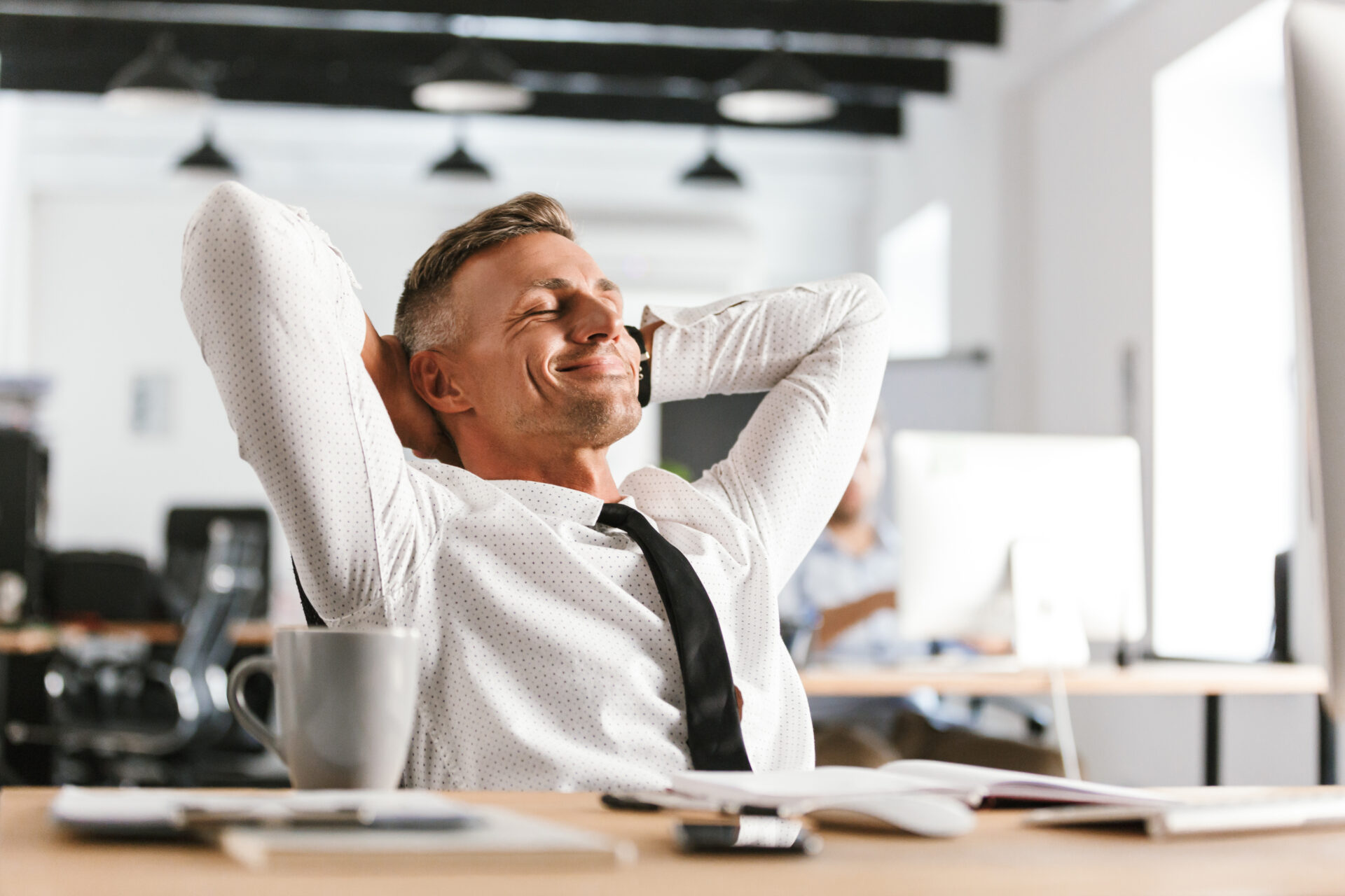 Image of Pleased middle aged business man relaxing while sitting by the table in office